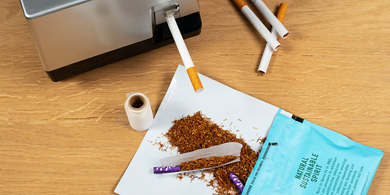 Drehtabak und Stopfmaschine mit Zigarettenhülsen, Tabak und Papier auf einem Holztisch