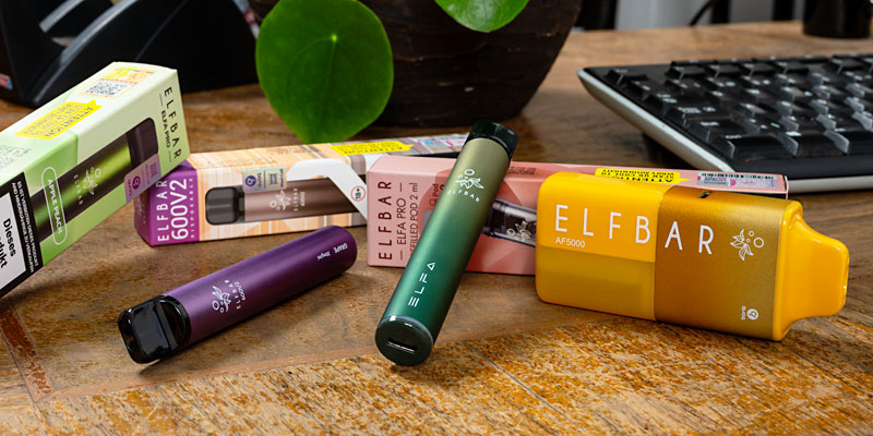 Eine Sammlung von Elf Bar Vapes in verschiedenen Farben und Verpackungen, die auf einem Holztisch ausgestellt sind.