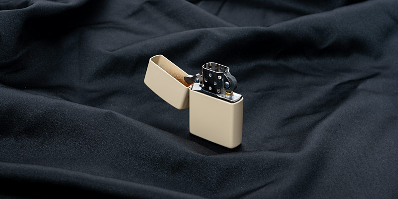 Ein geöffnetes beiges Zippo-Feuerzeug, stehend, auf einem schwarzen Stofftuch. 
