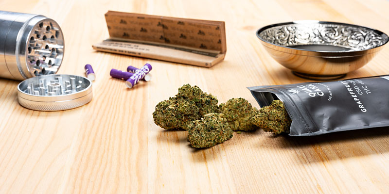 Häufig gestellte Fragen zu Qualicann: Bild mit CBD-Blüten, geöffneter Packung Qualicann-Blüten, Filter, Grinder, Zigaretten-Papier und Tellerchen 