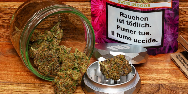 Qualicann-CBD-Blüten: Glas und Packung geöffnet auf Holzstrunk.