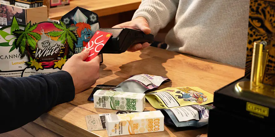 Verkaufsbereich mit CBD-Produkten im Smokee Baden. Ein Kunde bezahlt mit Karte, auf dem Tresen liegen diverse CBD-Drops und Hanfprodukte.