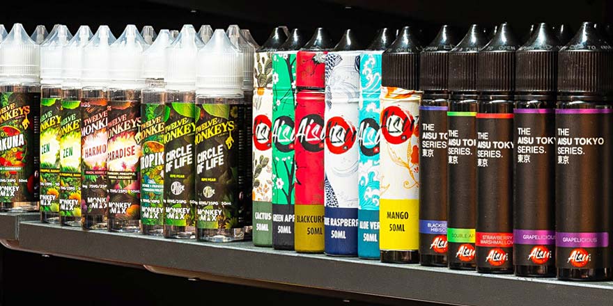 Nahaufnahme eines Regals mit zahlreichen E-Liquids und Nikotinsalzen im Smokee Baden, darunter Marken wie Twelve Monkeys, Aisu oder Dinner Lady.