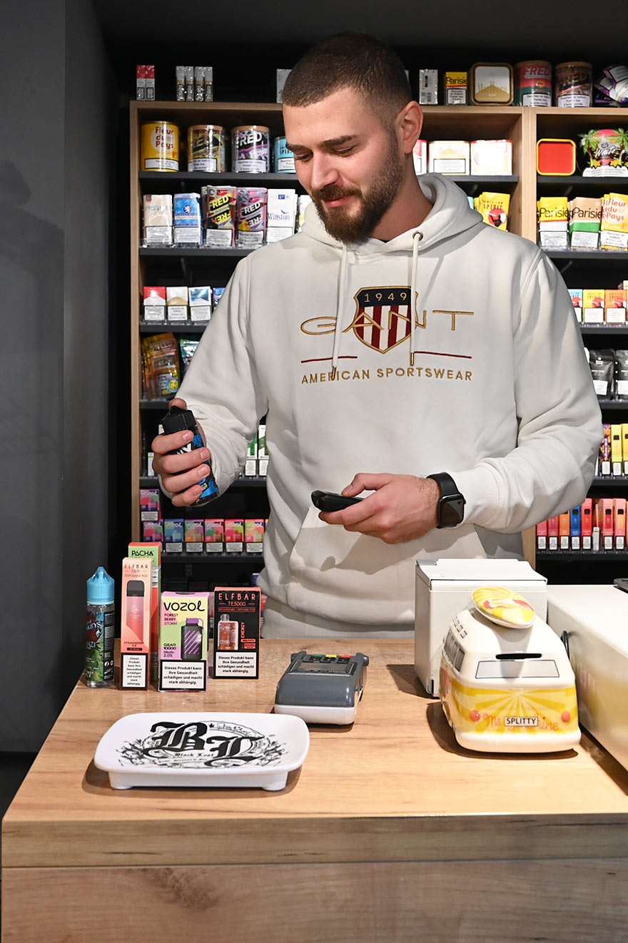 Mitarbeiter präsentiert Einweg-Vapes von Elfbar, Vozol und anderen Marken im Smokee Luzern