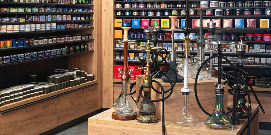Mehrere Shishas auf einem Holztisch vor Regalen mit Shisha-Tabak
