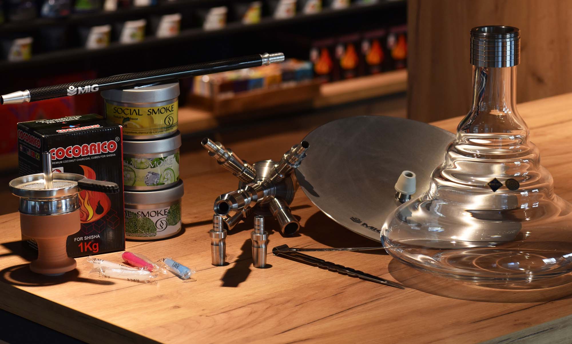  Shisha-Zubeh&ouml;r auf Holztisch: Bowl, Kopf, Kohle, Aufsatz, Edelstahlteile, Zange, Mundst&uuml;cke und Tabakdosen im Shop