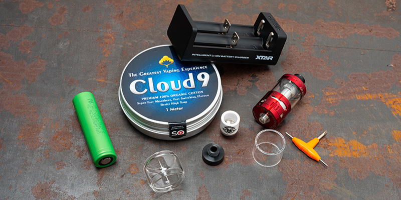 Eine Sammlung von Vaping-Zubeh&ouml;r, darunter eine Batterie, ein Ladeger&auml;t, eine Flasche E-Liquid, ein Beh&auml;lter mit Vaping-Watte, ein Werkzeug und ein Beh&auml;lter mit der Aufschrift &laquo;Cloud9&raquo;.